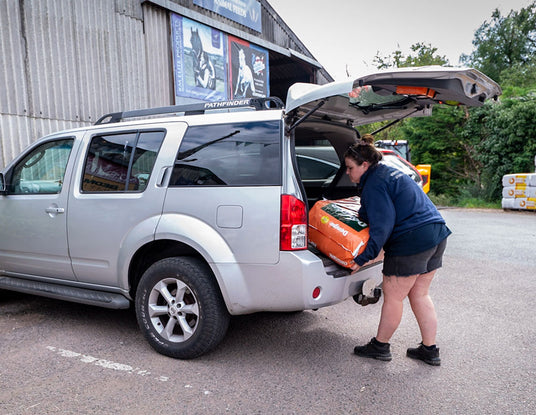 Person loading an orange toolbox into the back of a silver SUV.