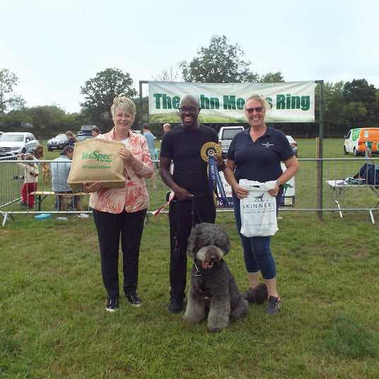 Three people with a dog at an outdoor event, holding bags with visible branding.