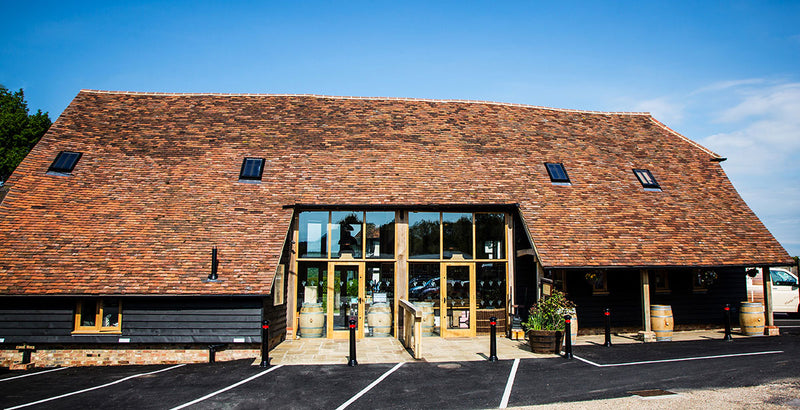 Large barn-style building with a red tiled roof and large windows, set against a blue sky.