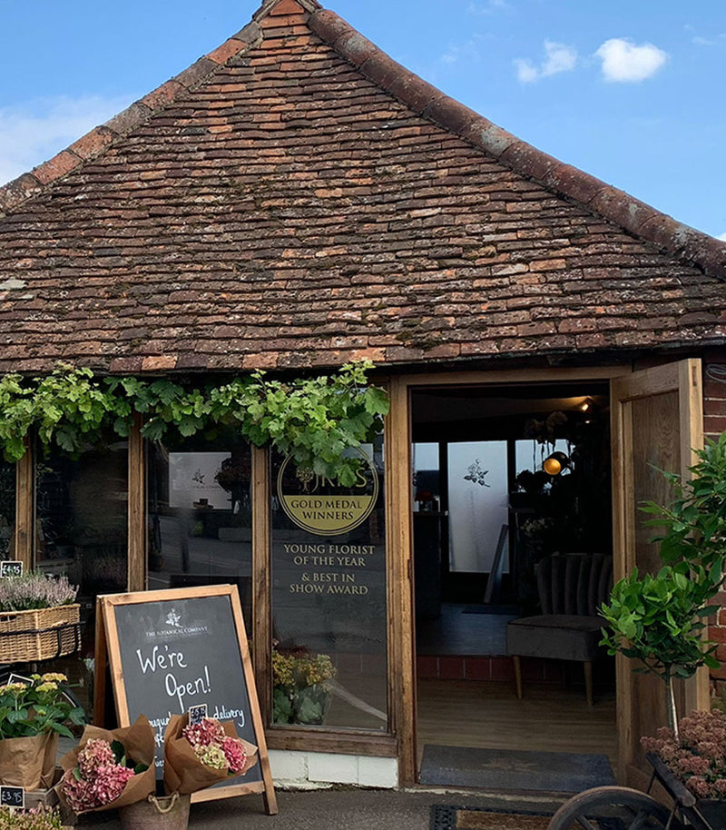 Wooden building with a thatched roof, sign for 'Young Florist of the Year' award, and open door.