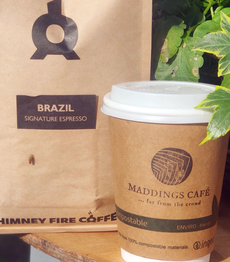 Brown paper cup with Madding's Cafe logo next to a cardboard coffee bag with 'Himney Fire Coffee' branding.