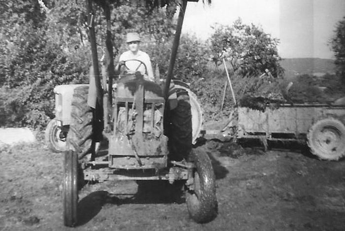 black and white photo of a person on a tractor with trees and a building in the background